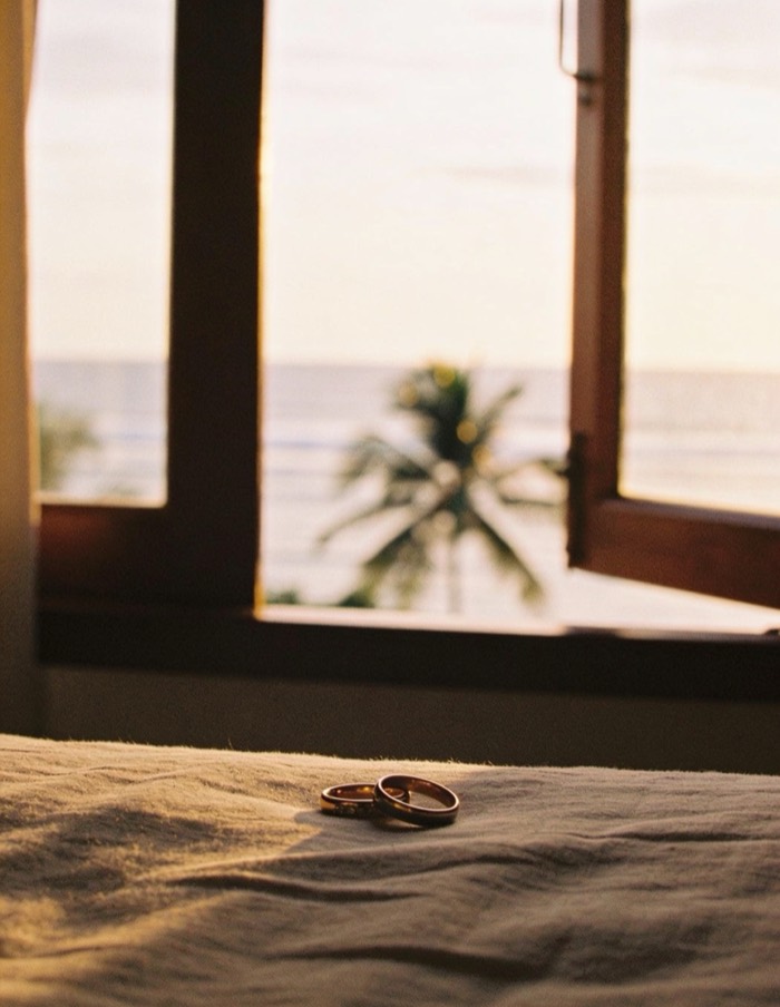 Duas alianças sobre a cama de um quarto com janela aberta para o mar